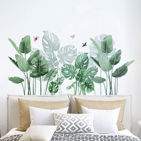 Groene palm- en monstera-bladeren met drie insecten op een witte muur, boven een wit bed met kussens.