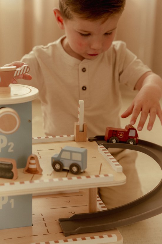 Kind speelt met een houten parkeergarage, met een rode brandweerwagen op de baan.