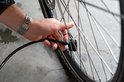 Hand met zilverkleurig horloge bevestigt de slang van een zwarte fietspomp aan een fietsventiel.