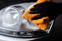 Hand met zwarte handschoen die auto koplamp poetst met oranje microvezeldoek.