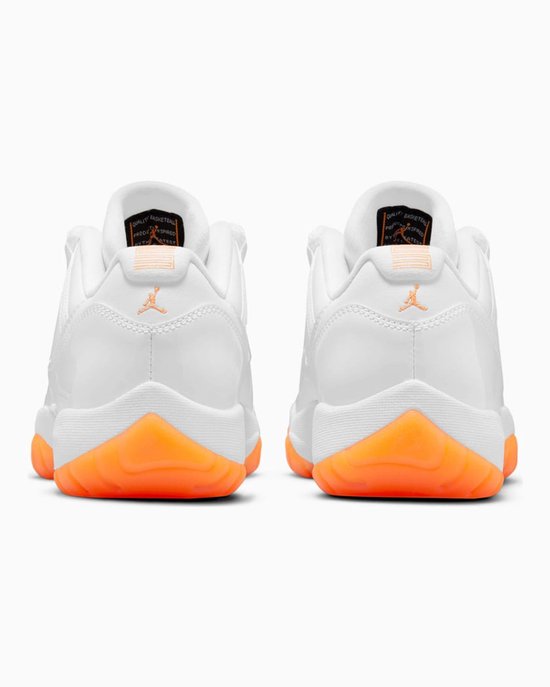 Achterkant van witte lage Air Jordan 11 sneakers met oranje Jumpman logo's en buitenzolen.