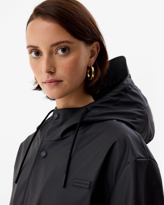 Close-up van een vrouw met gouden oorbellen in een zwarte, glanzende regenjas met capuchon.