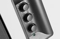 Close-up van de bedieningsknoppen voor treble, bas en volume op een donkergrijze speaker.