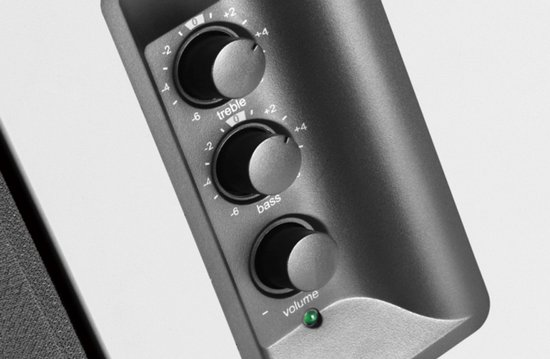 Close-up van de bedieningsknoppen voor treble, bas en volume op een donkergrijze speaker.