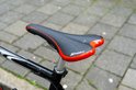 Zwart fietszadel met rode accenten, "SPORT" tekst en ventilatiegaatjes, op een fiets.