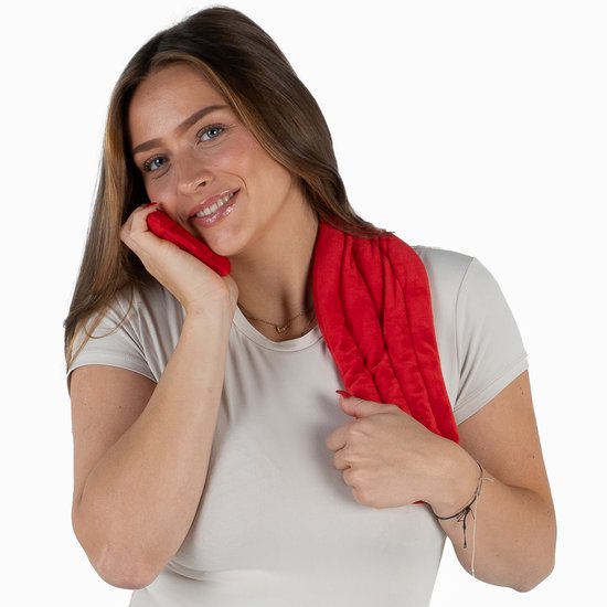 Jonge vrouw met een beige T-shirt houdt een rode Chillaxy warmtekussen tegen haar nek en borst, glimlachend.
