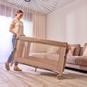 Beige reiswieg die wordt opgevouwen door een vrouw in een woonkamer.