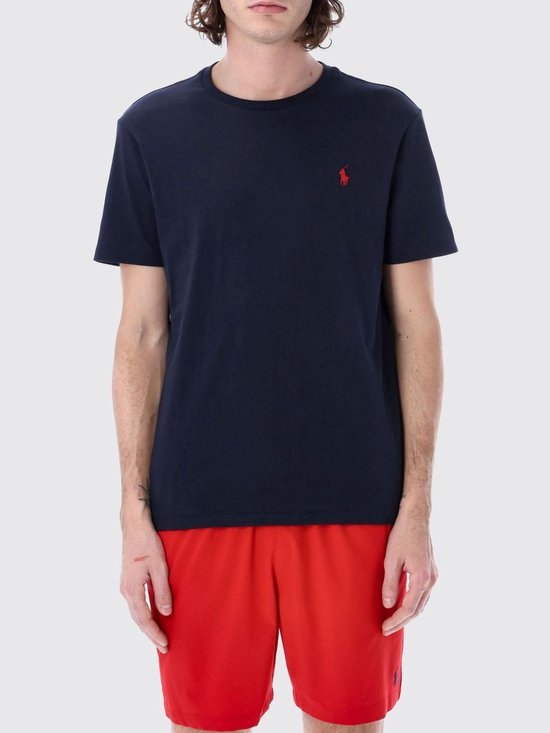 Model draagt een donkerblauw Polo Ralph Lauren T-shirt en rode korte broek.
