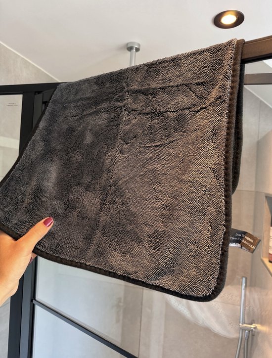 Main tenant une lingette microfibre gris foncé dans une cabine de douche.