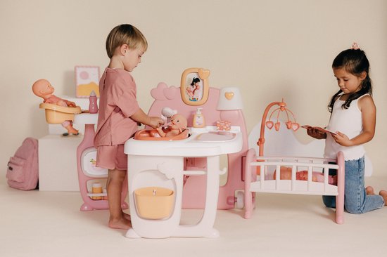 Jongen en meisje spelen met roze poppenverzorger. De jongen wast de pop, het meisje leest bij de wieg.