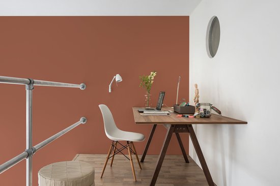Werkplek met terracotta muur, houten bureau en witte stoel.