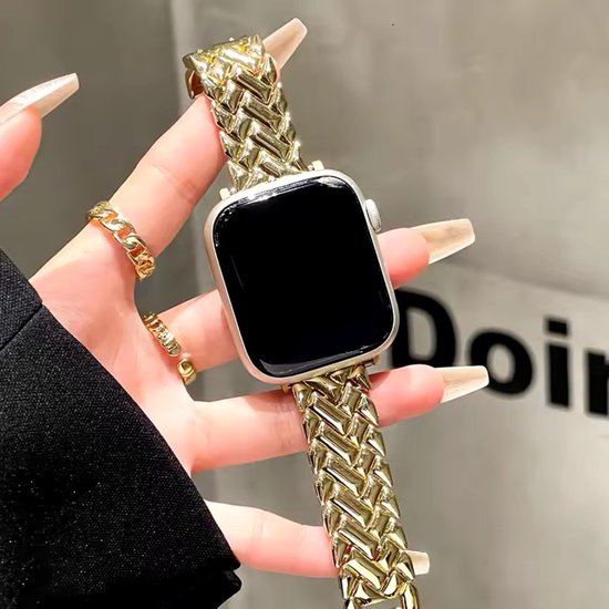 Gouden metalen Apple Watch bandje met visgraatpatroon, gedragen door een hand met gouden ringen.