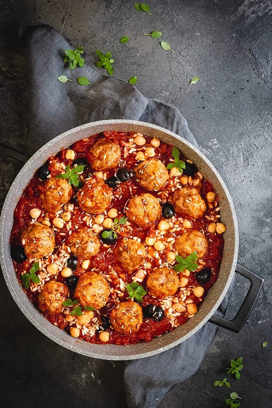 Kookpot met gehaktballetjes in tomatensaus, kikkererwten en olijven. Gegarneerd met peterselie.