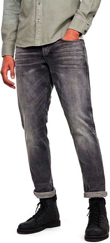 Man met lichtgrijze, gescheurde jeans met opgerolde pijpen en een lichtgroen shirt.