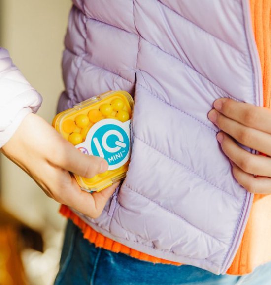 Hand in paarse jas stopt een geel IQ Mini spel met oranje balletjes in de zak.