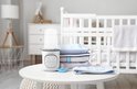 Witte Lionelo flesverwarmer met display op een tafel naast gestapelde babykleding en een speen.
