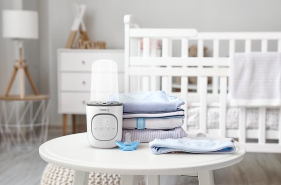 Witte Lionelo flesverwarmer met display op een tafel naast gestapelde babykleding en een speen.