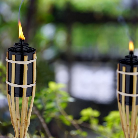 Twee bamboe tuinfakkels met zwarte houder en witte banden, brandend in een groene tuin.