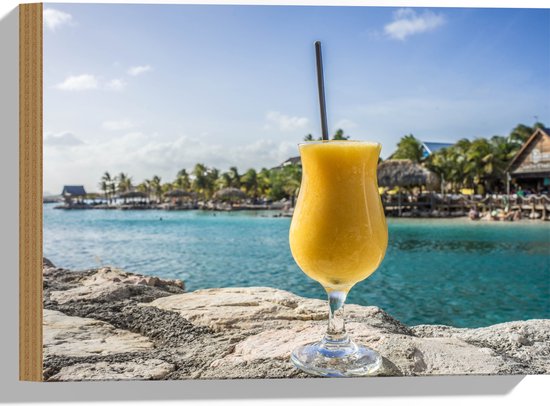 WallClassics - Hout - Gele Cocktail op Rots aan het Water van Vakantieplek - 40x30 cm - 9 mm dik - Foto op Hout (Met Ophangsysteem)