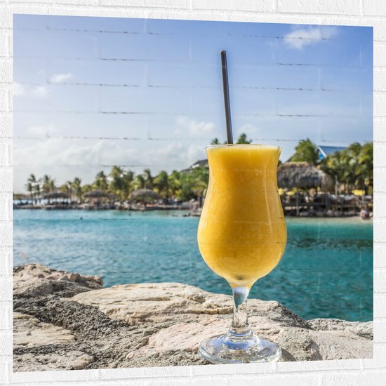 WallClassics - Muursticker - Gele Cocktail op Rots aan het Water van Vakantieplek - 100x100 cm Foto op Muursticker