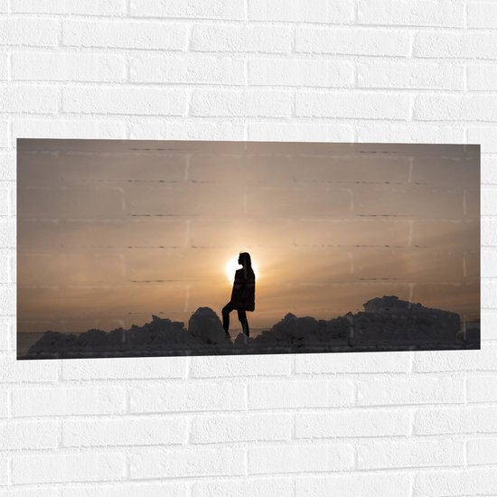 WallClassics - Muursticker - Silhouet van Vrouw op Hoop Sneeuw - 100x50 cm Foto op Muursticker