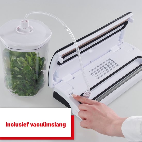Machine sous vide blanche avec couvercle ouvert, connectée à un récipient sous vide rempli de légumes-feuilles verts. Tuyau de vide inclus.