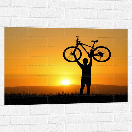 WallClassics - Muursticker - Silhouet van Man met Fiets bove Hoofd bij Feloranje Zonsondergang - 90x60 cm Foto op Muursticker