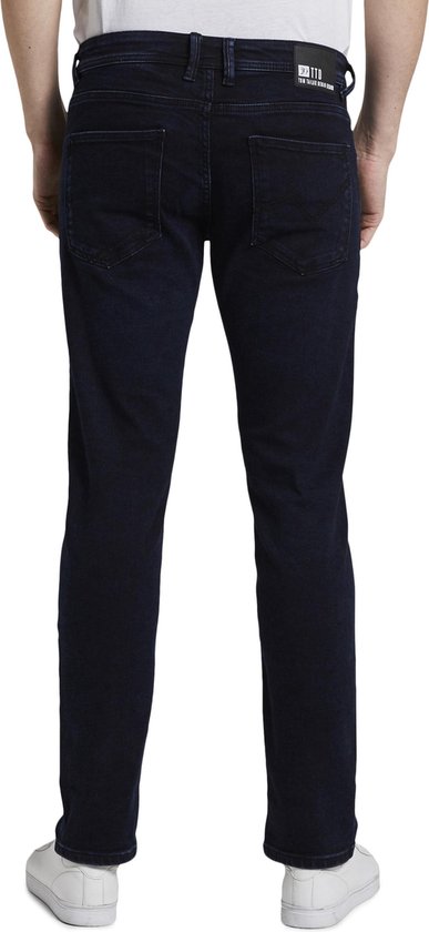 Achterkant van een man in een donkerblauwe slim fit jeans met achterzakken en een zwart label met 'TOM TAILOR DENIM BRAND'.