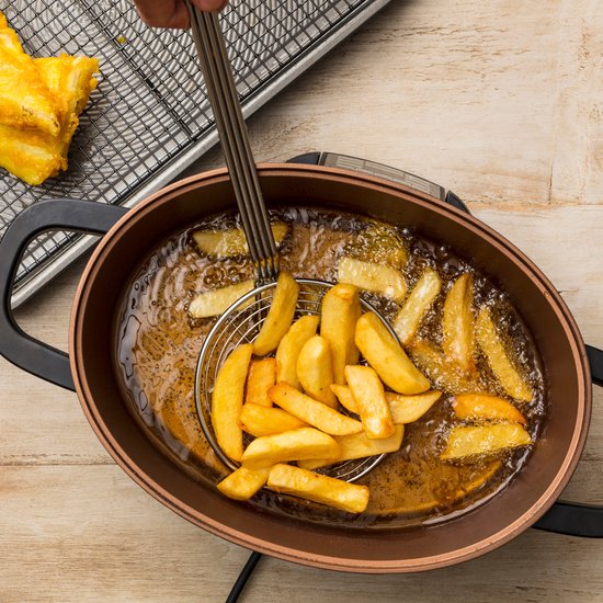 Frietjes worden uit een koperkleurige multicooker gehaald met een schuimspaan.