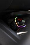 Zwarte Wegman Bluetooth FM-zender met gekleurde LED-verlichting, twee USB-poorten en een digitaal display, in een auto-console.