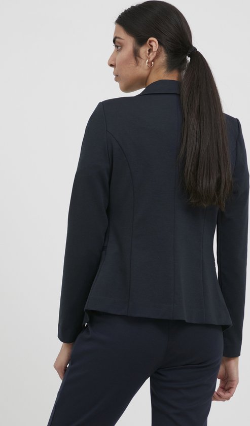 Achterkant van een vrouw met een paardenstaart, draagt een marineblauwe blazer en bijpassende broek.