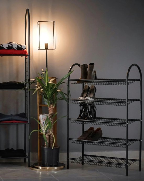 Zwart metalen schoenenrek met vier etages, gevuld met diverse schoenen, naast een plant.