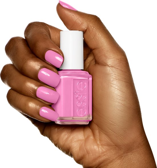 Hand met donkere huid met felroze Essie nagellak. Een flesje Essie nagellak in felroze wordt vastgehouden.