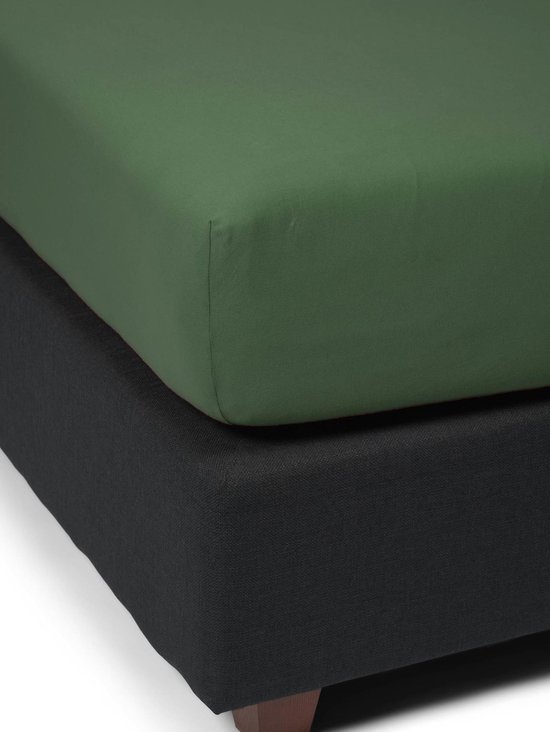Een mosgroen jersey hoeslaken gestapeld op een donkergrijs boxspring.