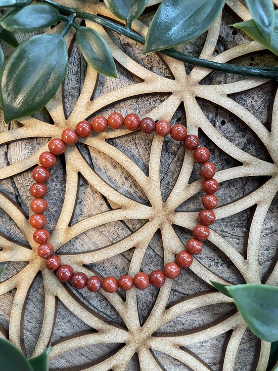 Een rood jaspis kinderarmbandje van 4 mm, met kralen, liggend op een houten ster.