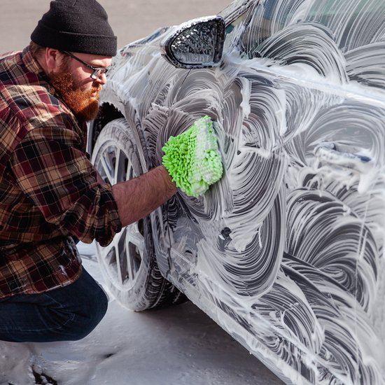 Man met baard wast een auto met een groene en witte spons.