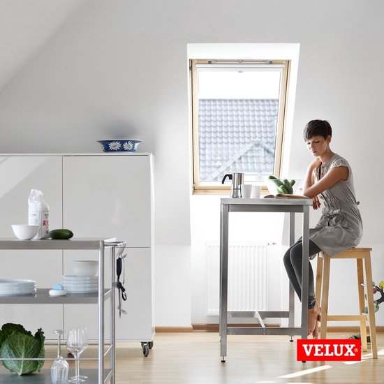 Cuisine avec fenêtre de toit VELUX. Une femme assise à une table. Logo VELUX.