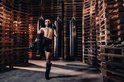 Een man met bokshandschoenen en scheenbeschermers in een vechtsport pose in een gymzaal.