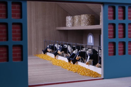 Speelgoedboerderij met zwart-wit koeien die eten uit een voerbak.