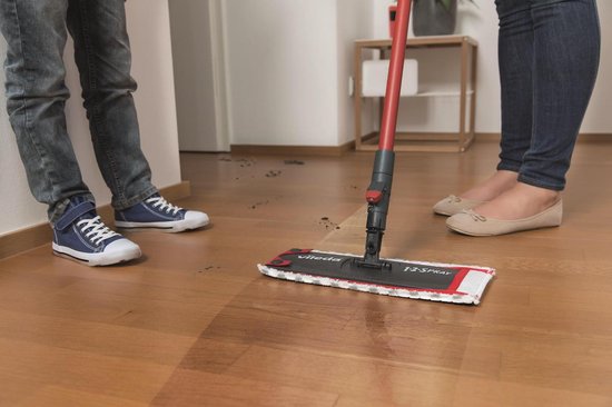 Detailopname van de Vileda 1.2. Spraymop in gebruik op een houten vloer, met benen van moeder en kind.