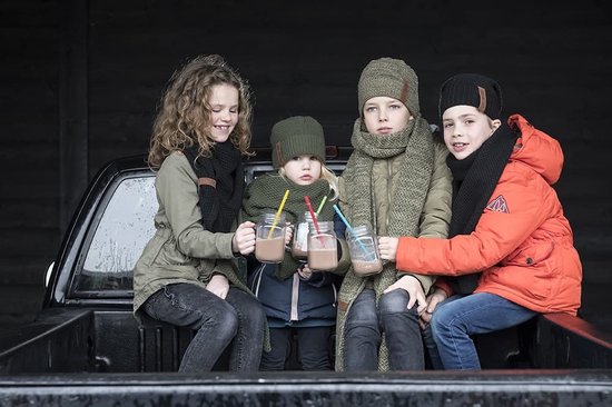 Vier kinderen met warme winterkleding en mutsen zitten op de achterbank van een pick-up truck en drinken uit mokken.