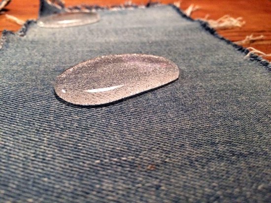 Transparante druppels water op een blauwe denim stof. De stof heeft rafelige randen.