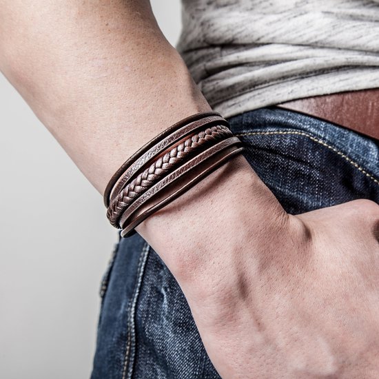 Bruine gevlochten en gladde leren armbanden van SERASAR met donkere sluiting, gedragen door een persoon in spijkerbroek.