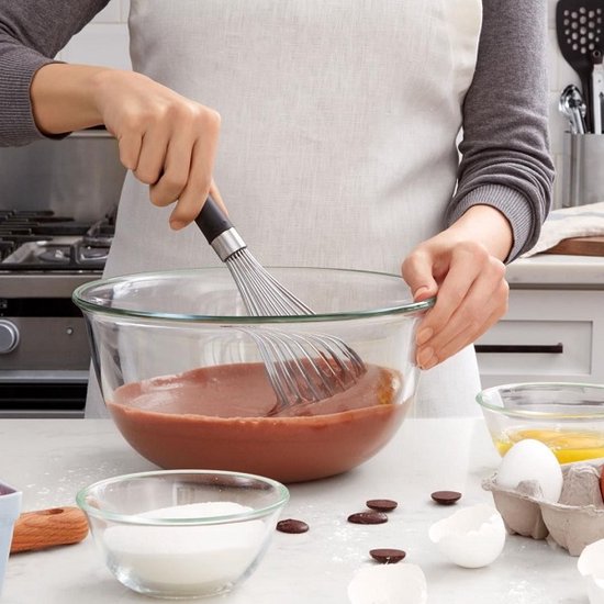 Personne portant un tablier utilisant un fouet OXO dans un bol en verre rempli de pâte à chocolat.