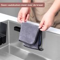 Een grijze vaatdoek met zwarte rand, wordt door handen aan een matzwarte vaatdoekhouder gehangen.
