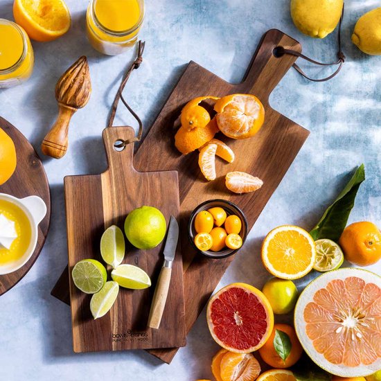 Walnotenhouten borrelplank, deels bedekt met citrusvruchten, kaas en vleeswaren.