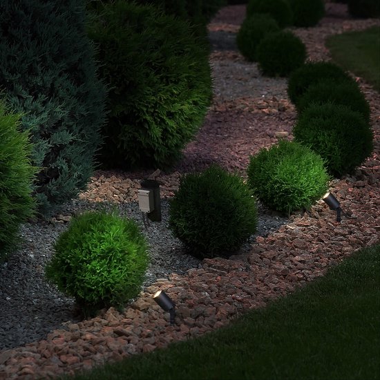 Zwarte LED-spots die een tuin met struiken en grind 's avonds verlichten.
