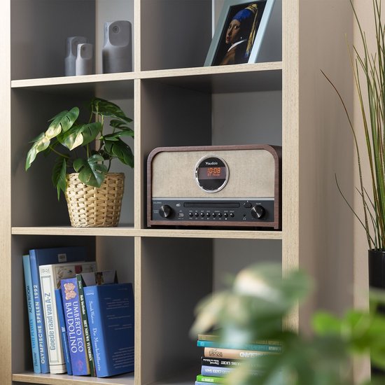Audizio Salerno radio met CD-speler staat op een plank in een boekenkast, naast planten en boeken.