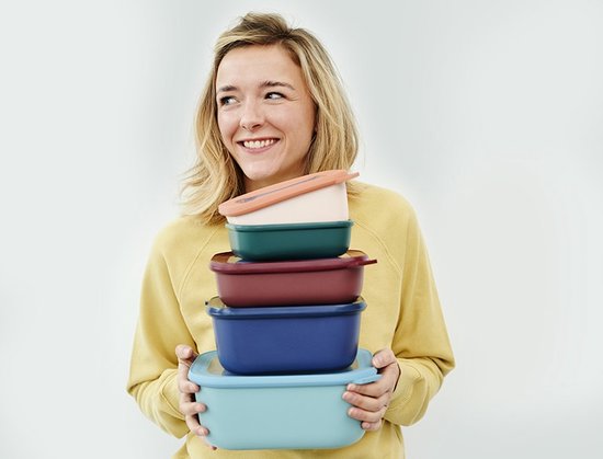 Femme souriante en pull jaune tenant une pile de cinq boîtes de conservation Mepal de différentes couleurs.
