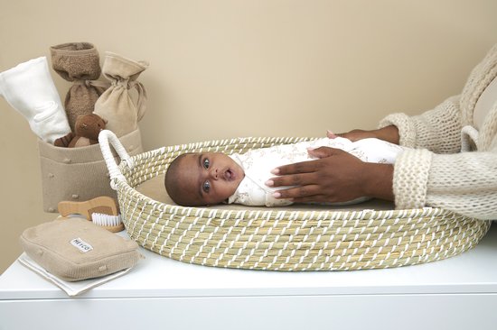 Baby in een wit Meyco inbakerdoek met takjesprint, liggend op een aankleedkussen.